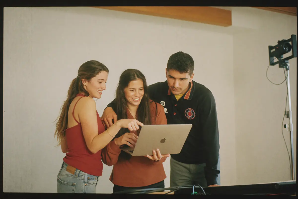 Three people around a laptop in a bright studio, working on something together.